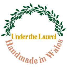 A round logo with a laurel wreath that states “Under the Laurel. Handmade in Wales”